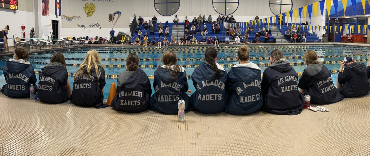 The AAHS girls swim team sits along the edge of the pool before competition,